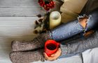 Warm and cozy,and warm concept girls feet in warm knitted socks with a Cup of tea over white wooden table with book and candle