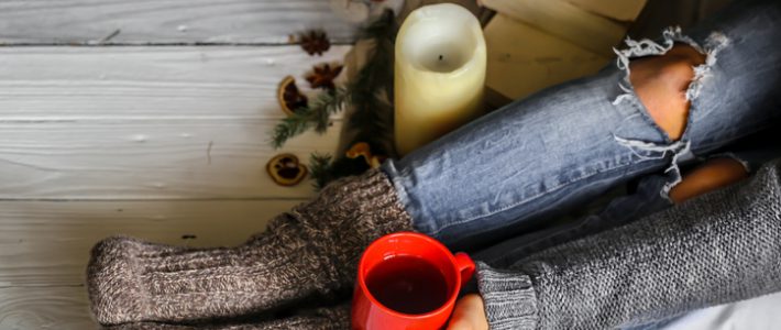 Warm and cozy,and warm concept girls feet in warm knitted socks with a Cup of tea over white wooden table with book and candle